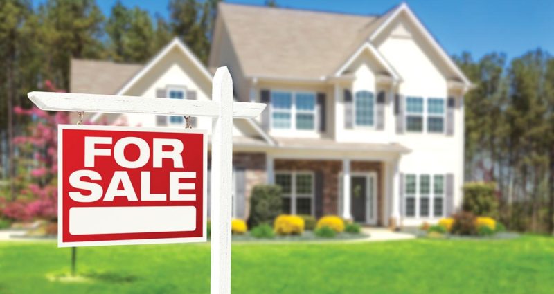 A red For Sale sign in front of a colonial-style two-story home.