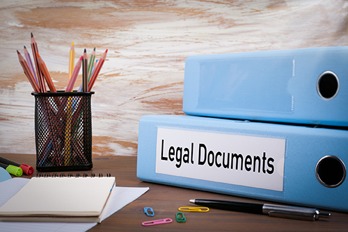 A binder of legal documents next to a container of pencils and a pad of paper.