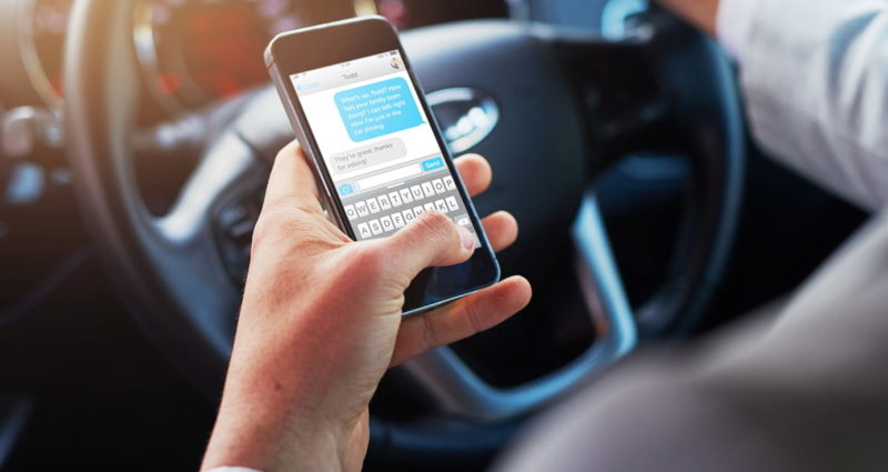 Closeup of a person texting on an iPhone while driving a vehicle