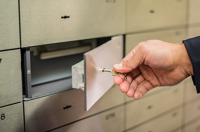 Closeup of a hand using a key on a bank lockbox to remove documents.