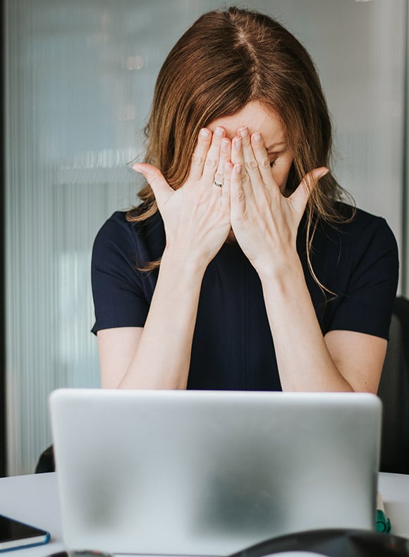 Distraught woman at a computer covering her face.