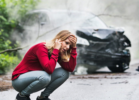 Woman crouched down on the phone in front of her smashed car