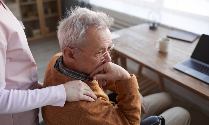 Elderly man in a wheelchair with a woman comforting him