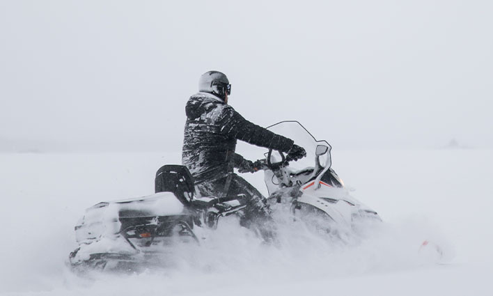 Man in black snow suit rides a snowmobile