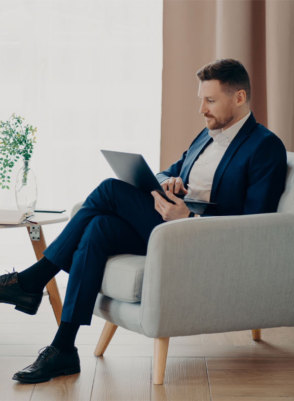 Concentrated Business Man Looking at Laptop in Grey Chair